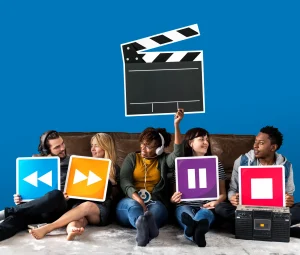 Group of friends sitting on couch holding colorful media control icons with movie clapperboard on blue background, representing video production and streaming