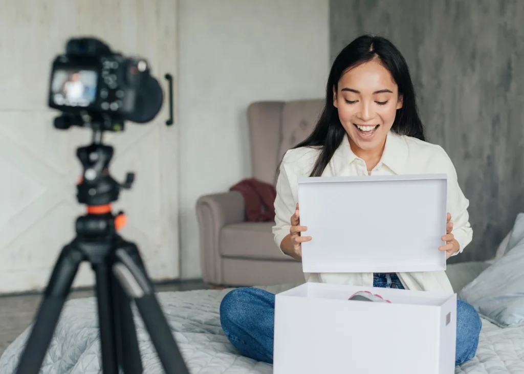 Smiling woman recording unboxing video for social media channel using digital camera on tripod