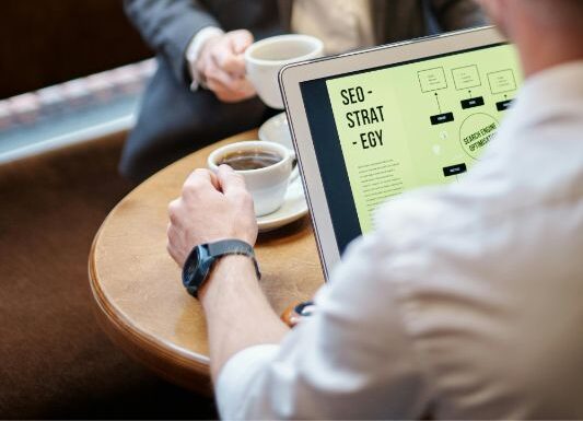 Person holding a cup of coffee and viewing a laptop displaying an SEO strategy — concept image for AI SEO company.