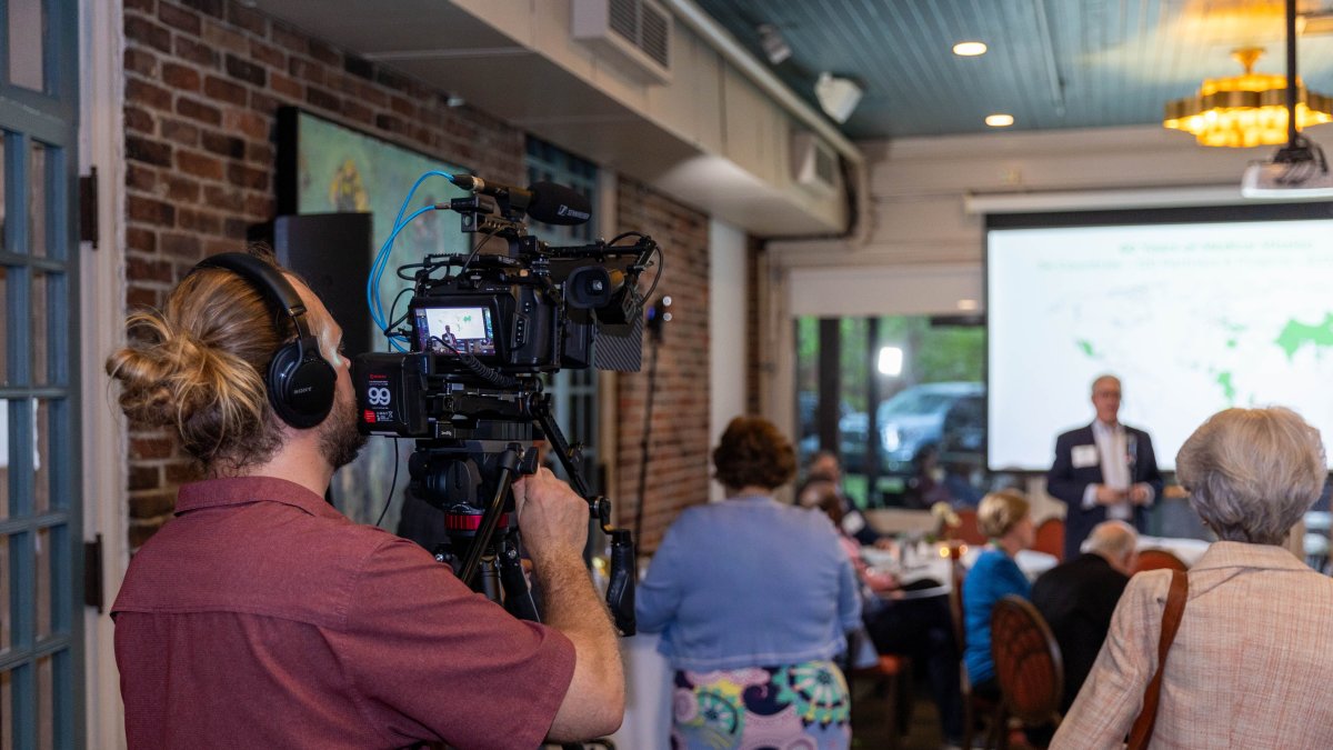 Videographer documenting a professional corporate event with attendees and projection screen